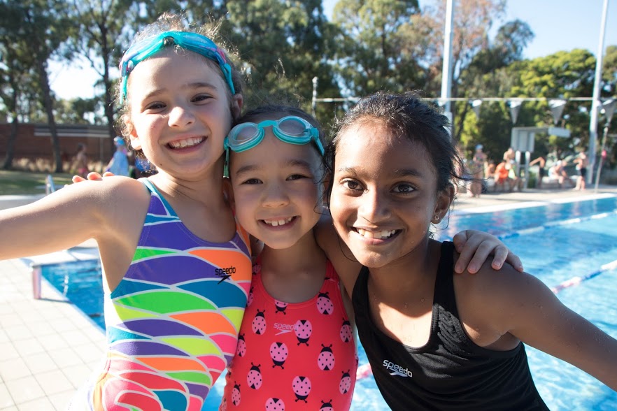 three girls hugging wearing googles in sun by pool