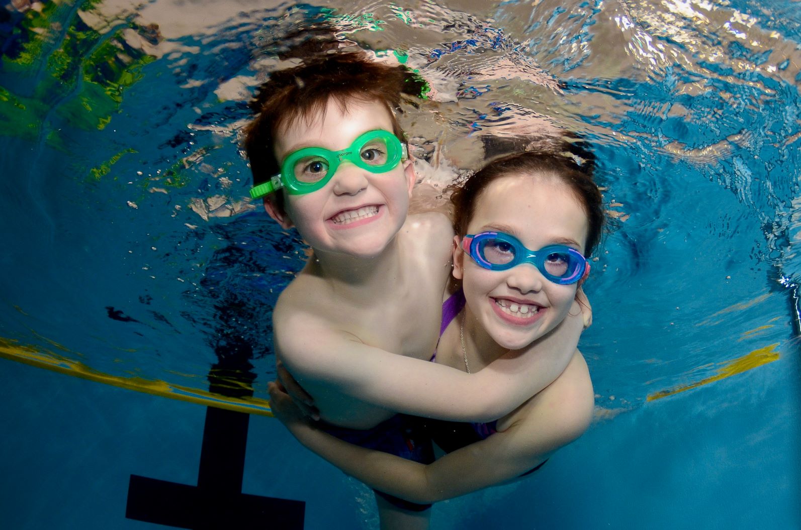 Brother and sister hugging and smiling underwater