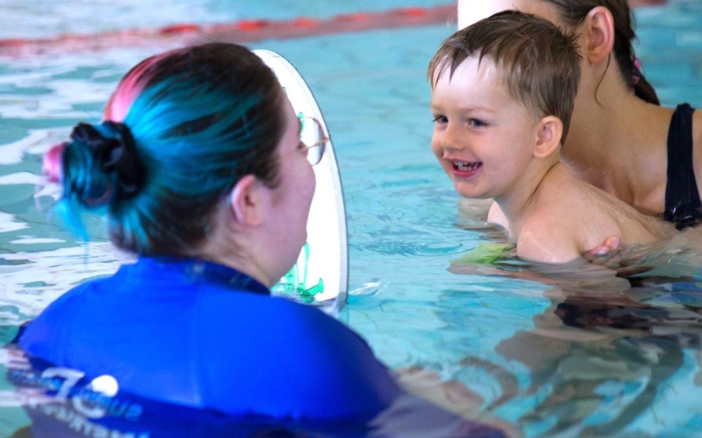 Toddler smiling at swim teacher holding mirror